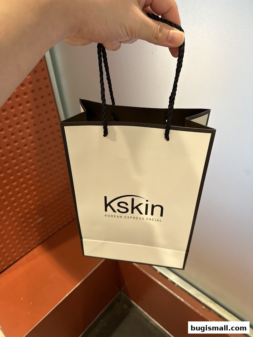 A hand holds a white shopping bag with the Kskin Korean Express Facial logo.