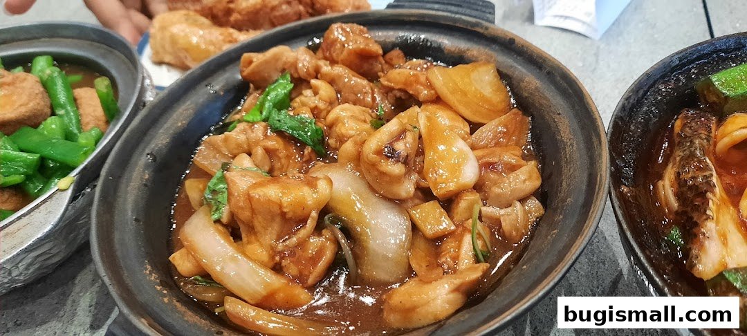 Close-up of claypot dishes featuring chicken, onions, and greens, with other dishes visible.