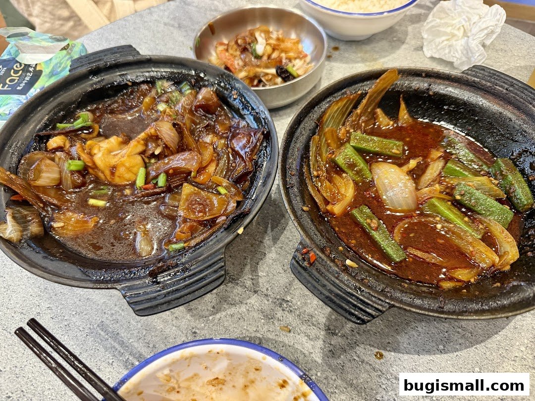 Two claypot dishes with fish, okra, and onions in a savory sauce, served with chopsticks.