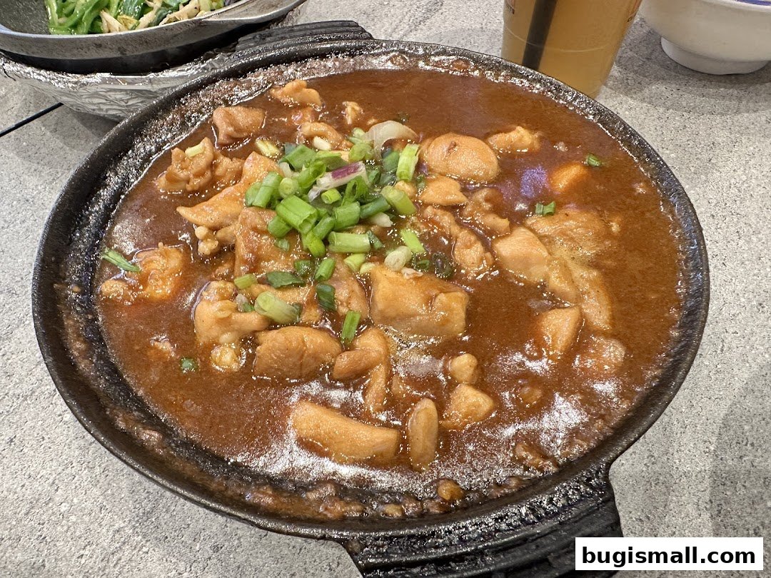 A close-up of a sizzling claypot dish with chicken and gravy, topped with green onions.
