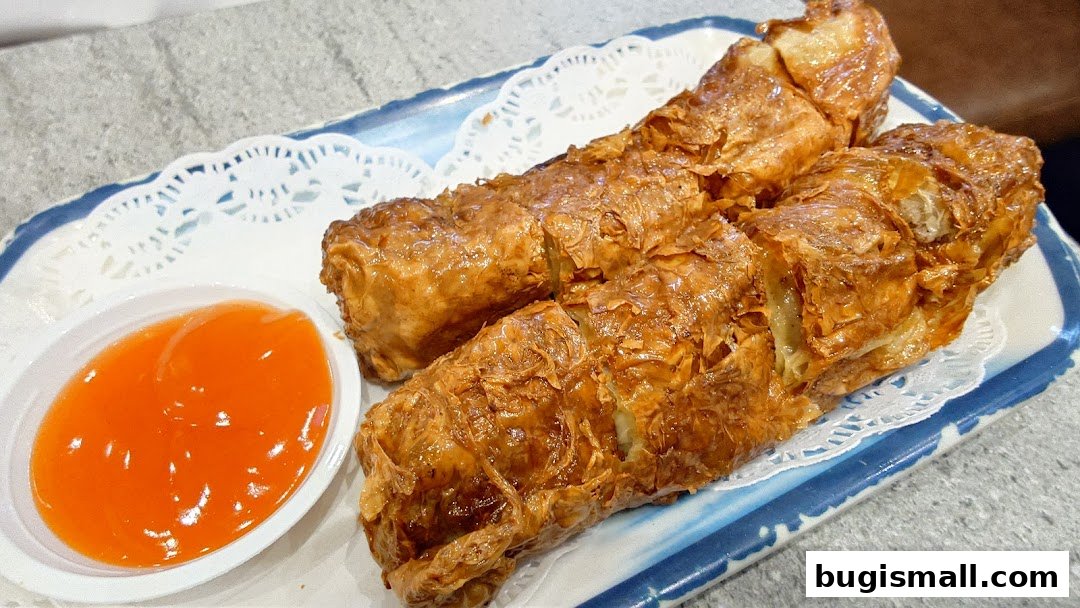 Crispy fried bean curd rolls served with a side of sweet chili sauce on a decorative plate.
