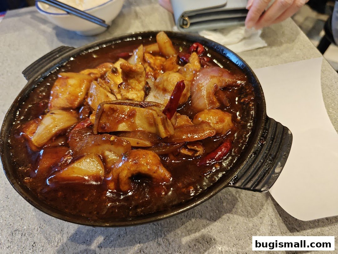 A close-up shot of a sizzling claypot dish with meat, onions, and chili peppers.