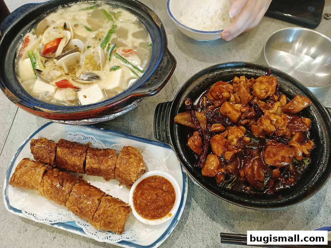 A spread of delicious claypot dishes and fried spring rolls with dipping sauce.