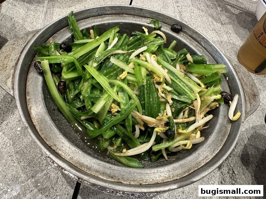 A close-up of a claypot dish with stir-fried green vegetables and bean sprouts.