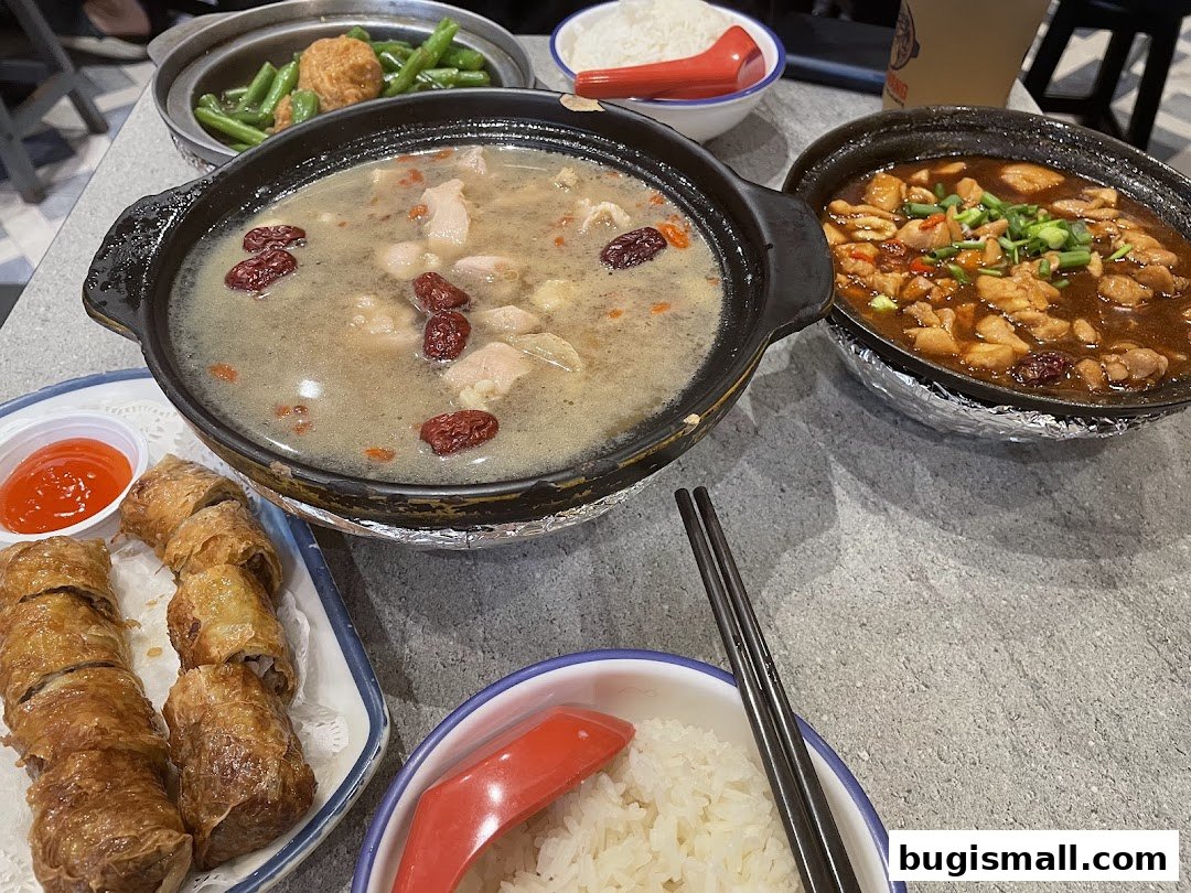 A table laden with delicious claypot dishes, rice, and spring rolls.