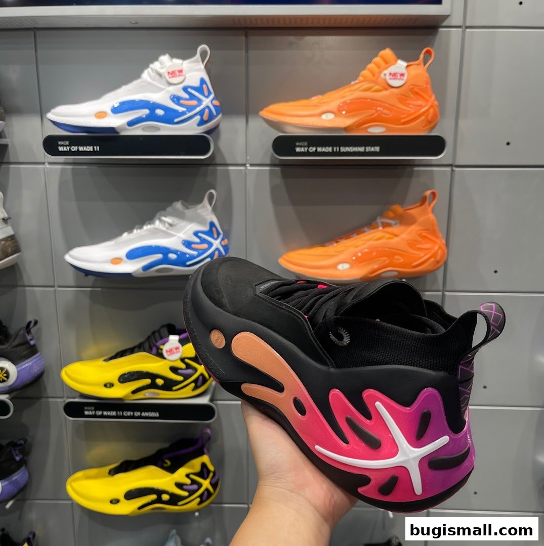 A hand holds a black and pink basketball shoe in front of a display of colorful Way of Wade 11 sneakers.