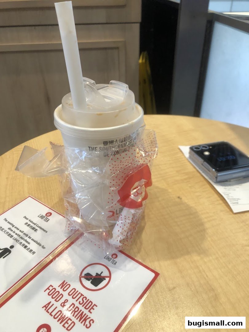 A LiHO TEA cup with a straw, wrapped in plastic, sits on a table with a sign.