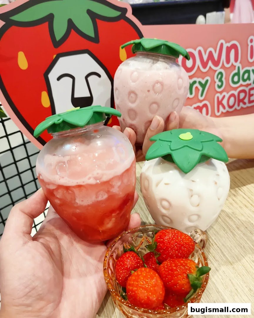 Hands holding strawberry-shaped drinks and a bowl of fresh strawberries.