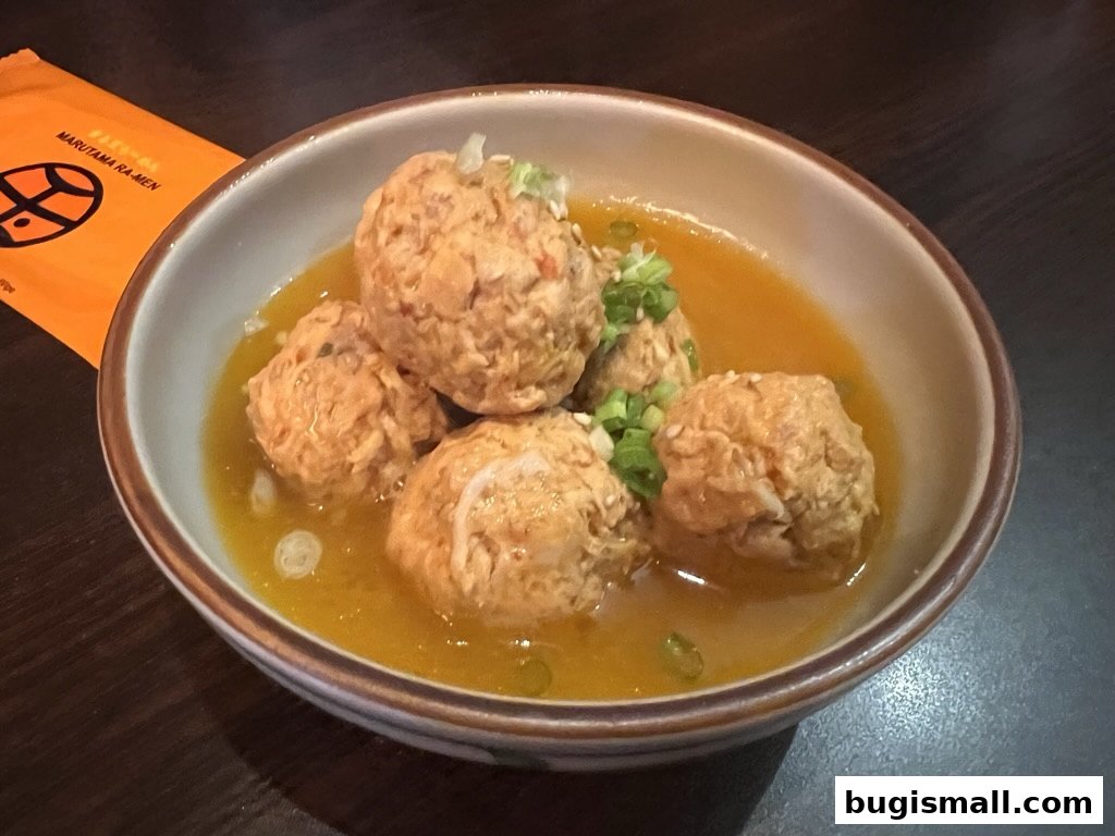 A bowl of Japanese chicken meatballs in broth, garnished with green onions and sesame seeds.