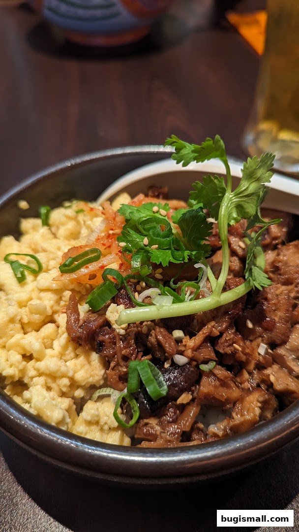 A close-up of a ramen dish with scrambled eggs, shredded meat, and garnishes.