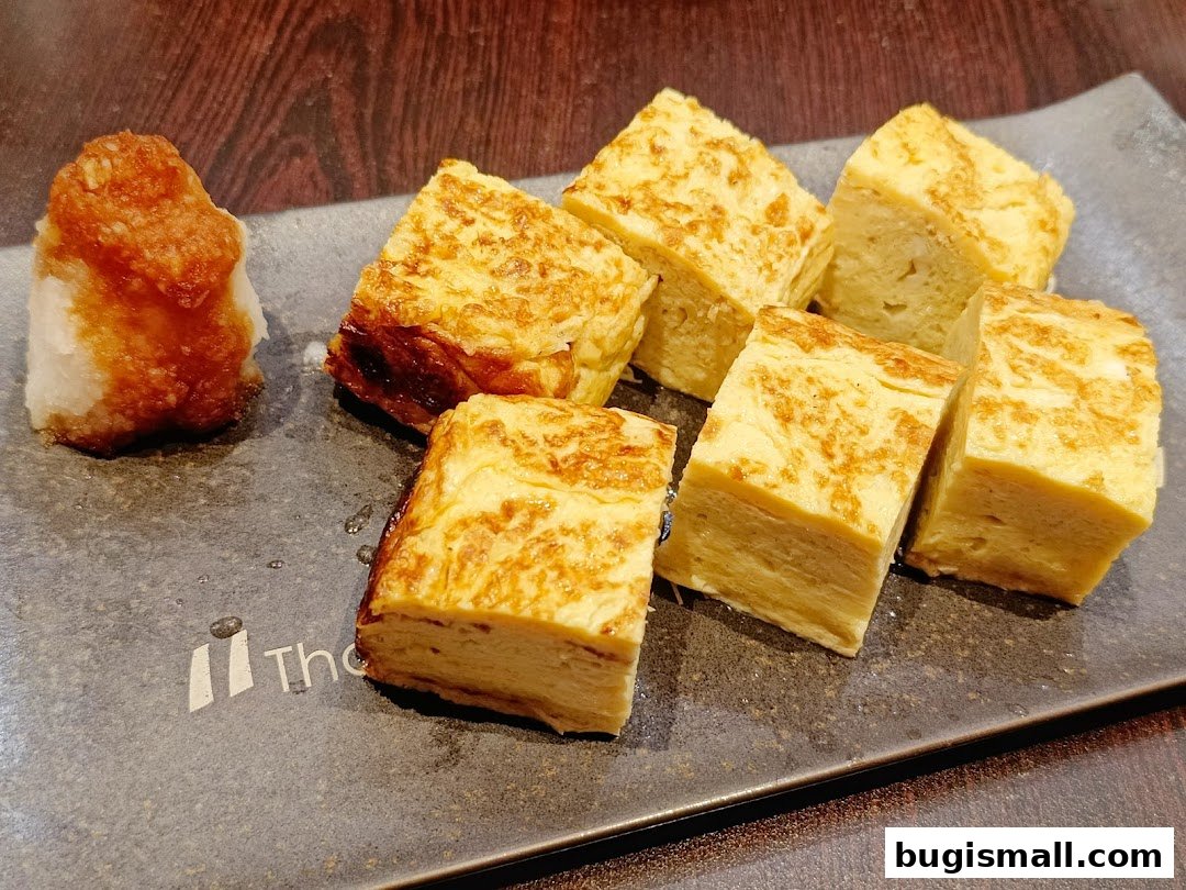 A close-up shot of tamagoyaki (rolled omelet) served with grated daikon radish and sauce.