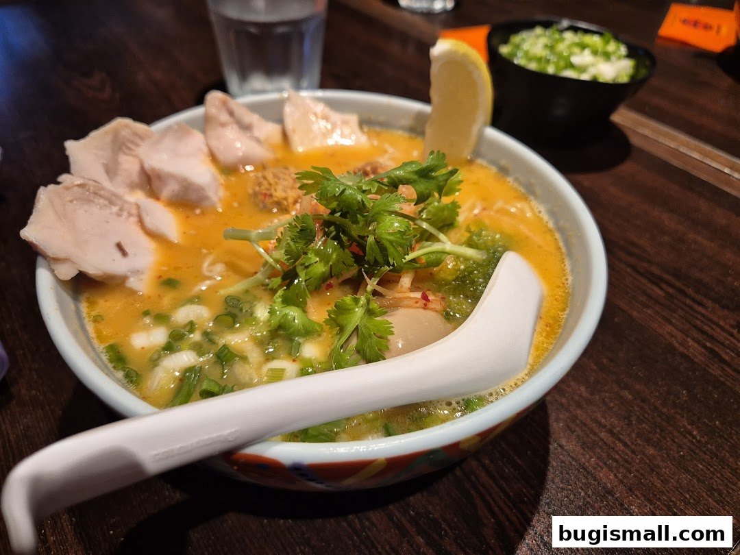 A close-up of a delicious bowl of ramen with chicken, cilantro, and a lemon slice.