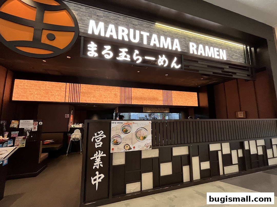 The entrance of Marutama Ramen Bugis with its illuminated sign and modern interior design.