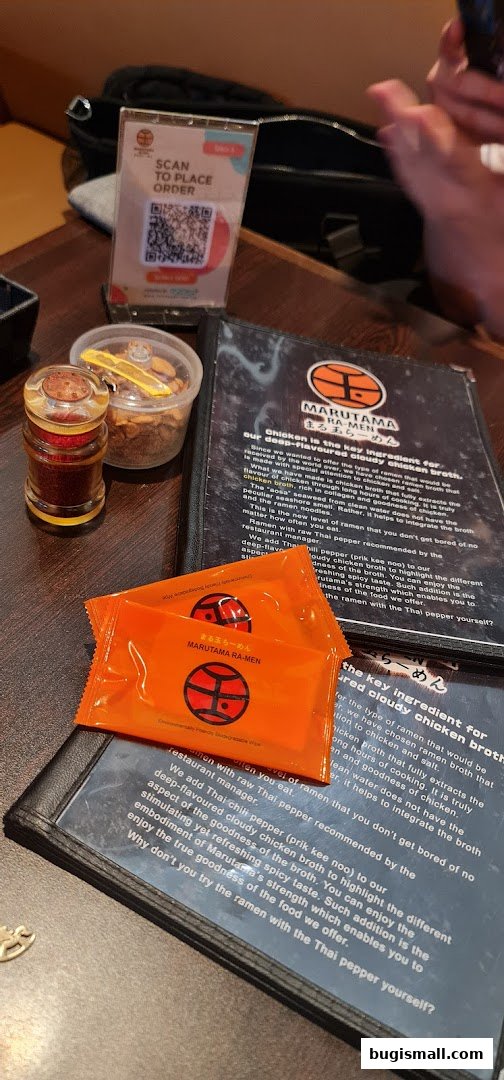A table setting at Marutama Ramen Bugis with menus, wet wipes, and condiments.