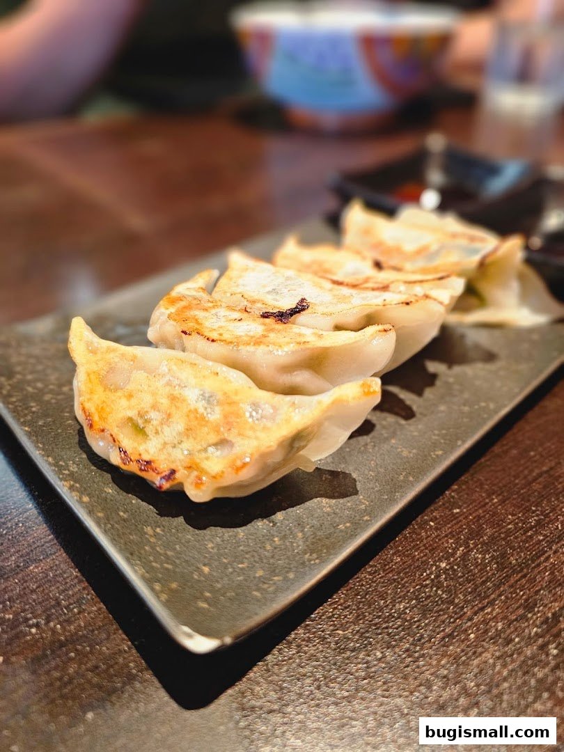 A close-up shot of pan-fried gyoza dumplings served on a dark rectangular plate.
