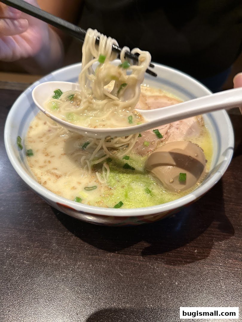 A close-up shot of a steaming bowl of ramen with noodles being lifted by chopsticks and a spoon.