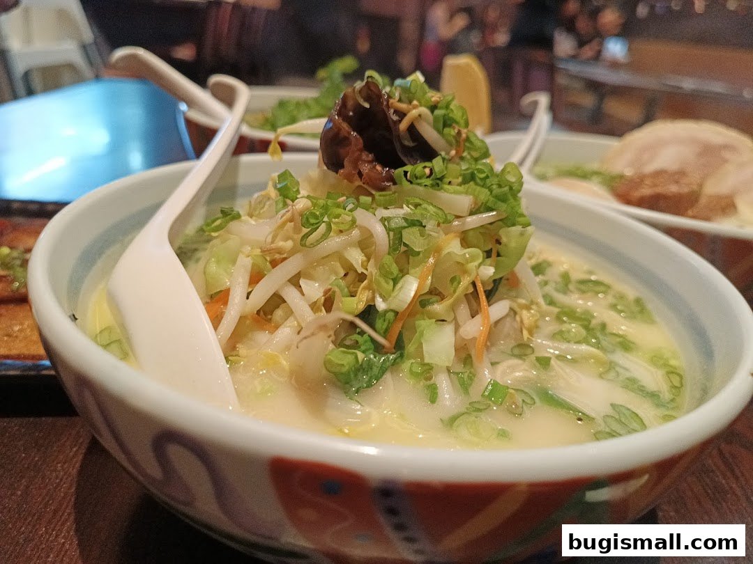 A close-up of a steaming bowl of ramen with fresh vegetables and a spoon.