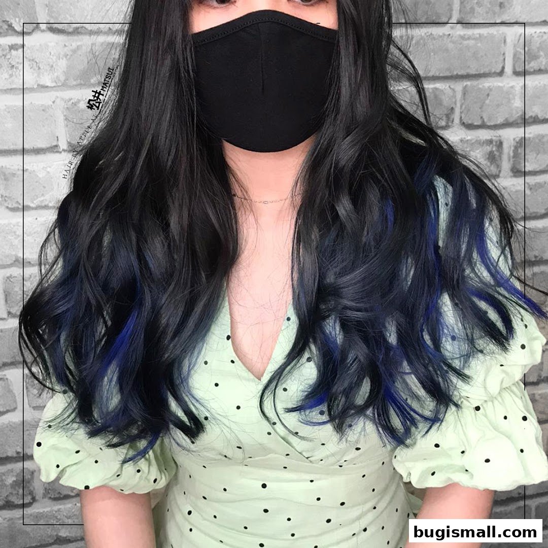 A person with long, wavy black hair with blue highlights, wearing a polka dot dress and a black mask.