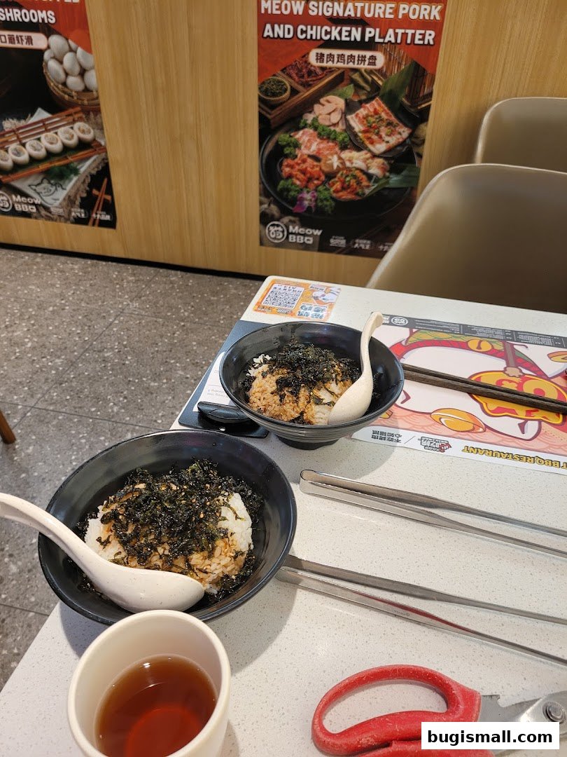 Two bowls of rice topped with seaweed and sesame seeds, a cup of tea, and barbecue utensils.