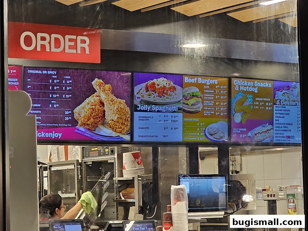 A digital menu board displaying various food items including fried chicken, burgers, spaghetti, and sides.