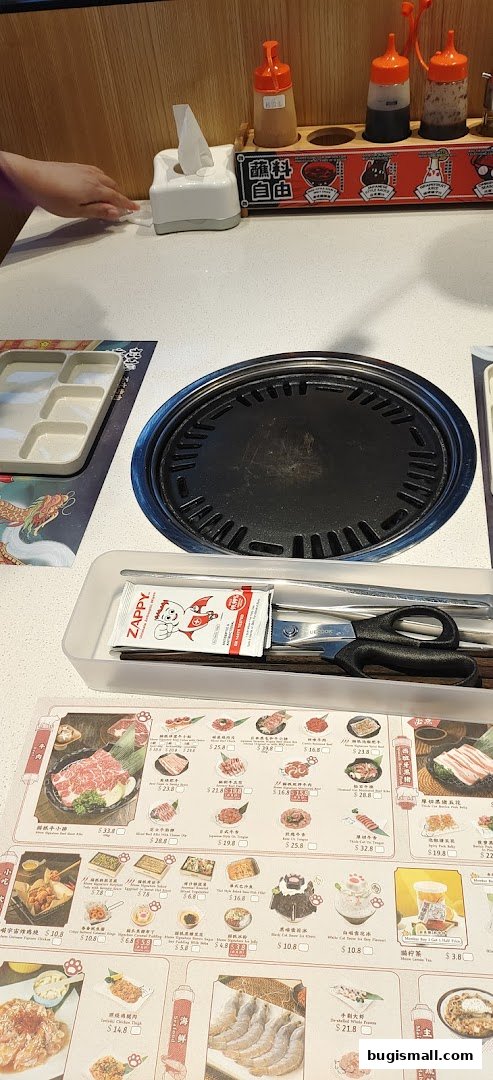 A table setting at Meow Barbecue with a grill, utensils, and a menu featuring various meat dishes.