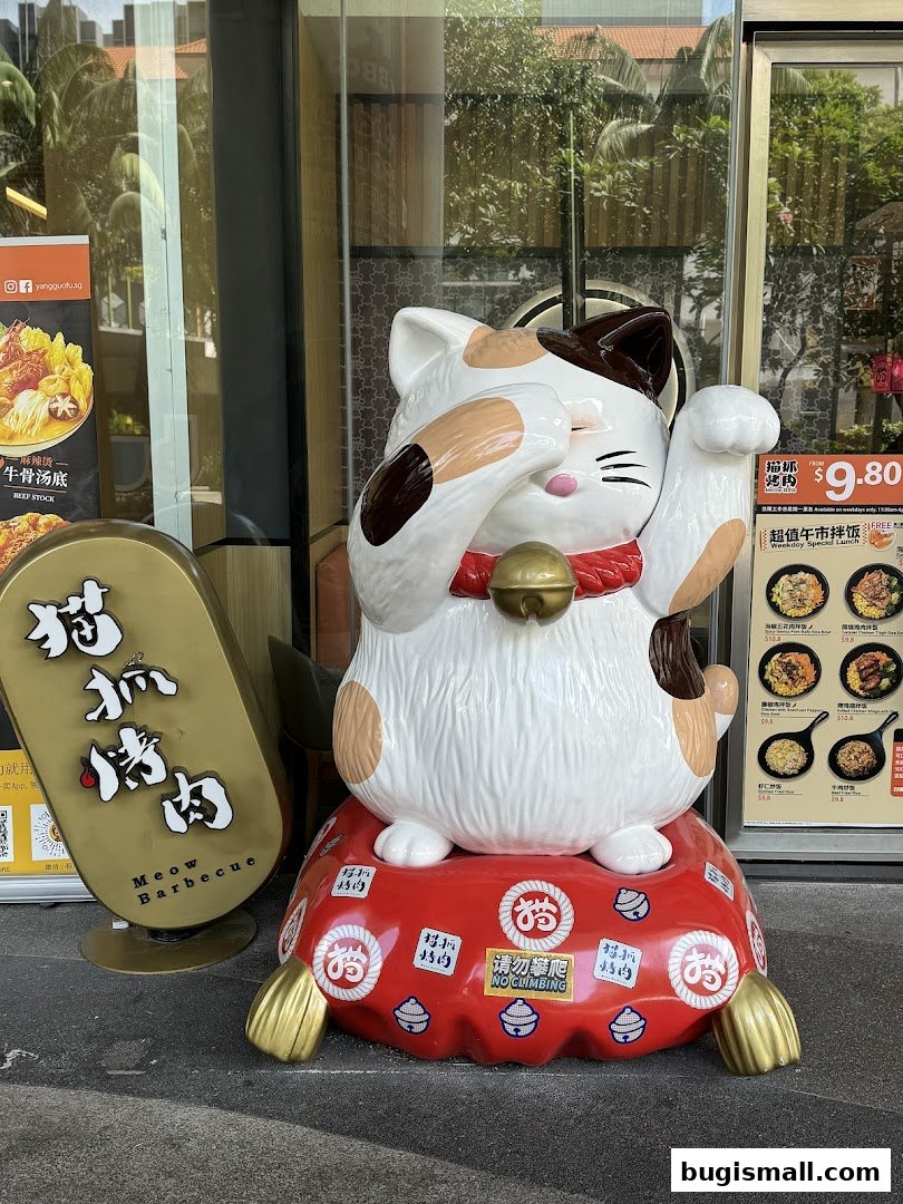 A large Maneki-neko statue sits outside a restaurant with a menu visible in the background.