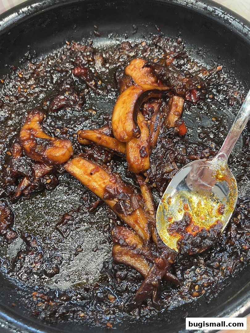A close-up of a dish with glazed ingredients and a spoon in a black bowl.