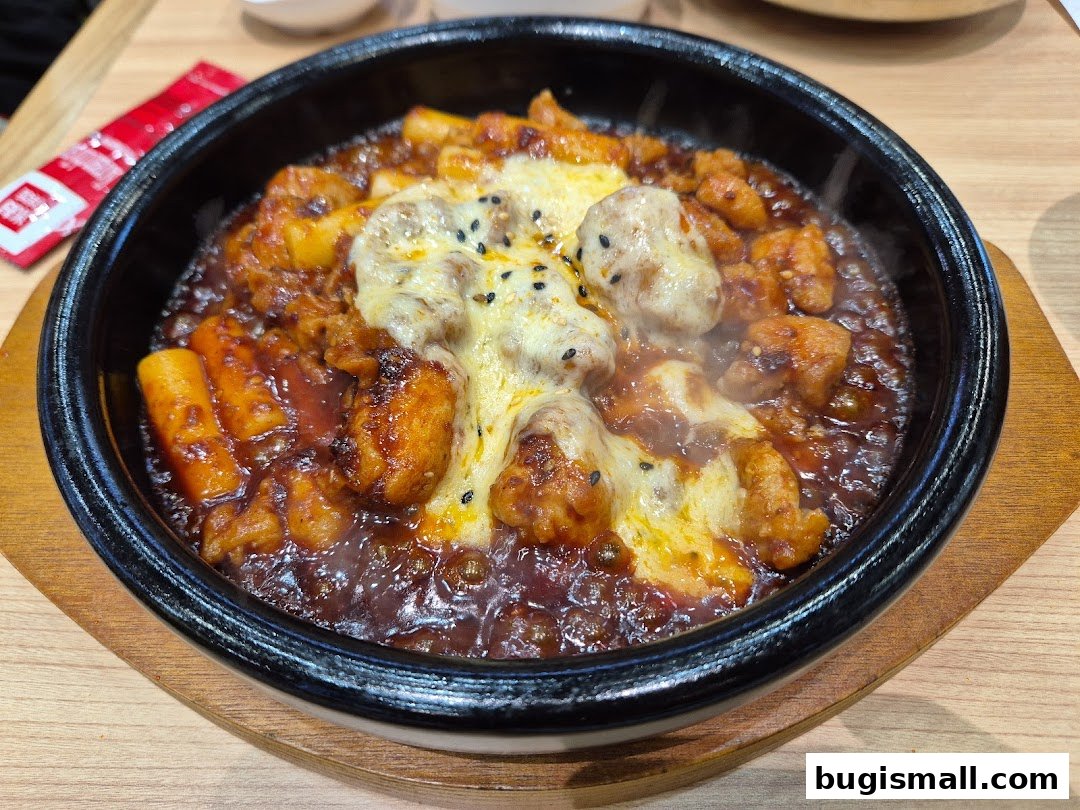 A close-up of a steaming dish of Korean fried chicken and tteokbokki topped with melted cheese.