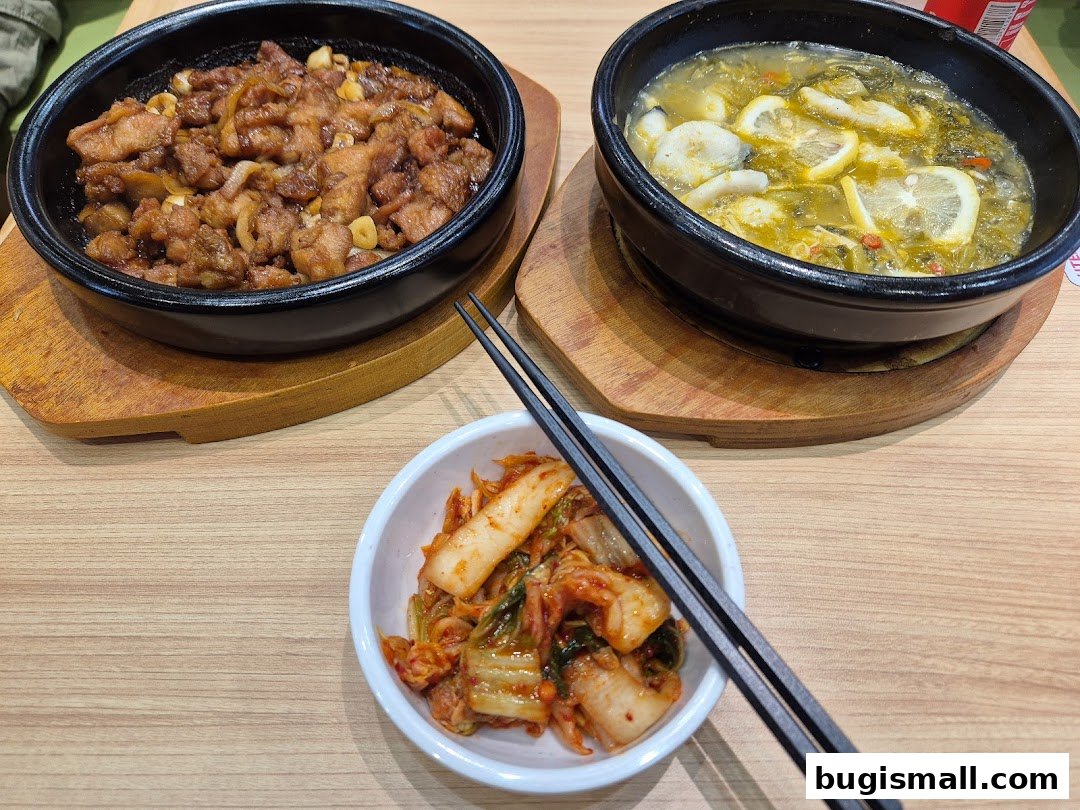 A close-up shot of Korean dishes, including a sizzling meat dish, a soup with lemon slices, and kimchi.