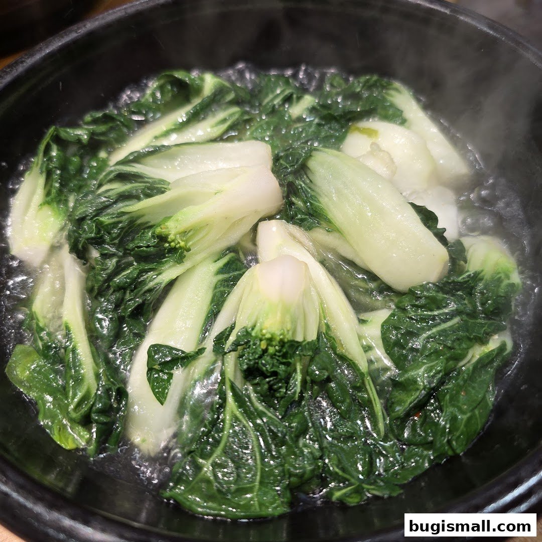 A close-up shot of fresh bok choy being steamed in a black pot.