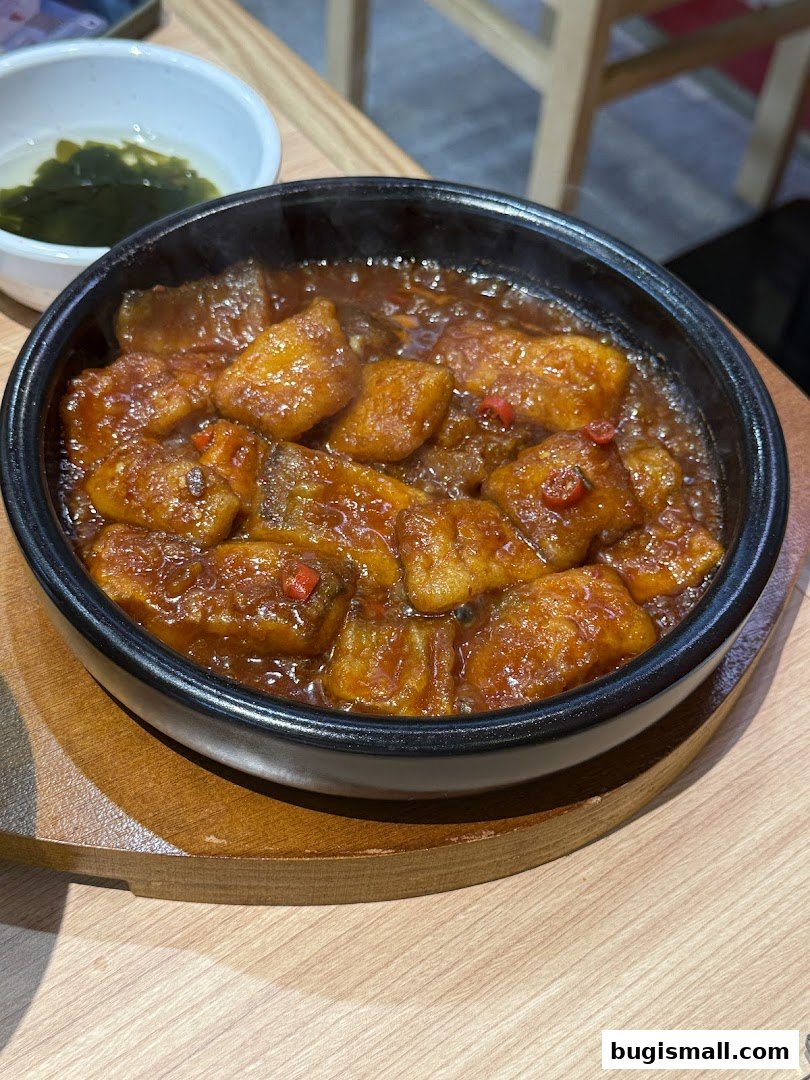 A close-up of a steaming hot dish of Korean braised fish with a side of seaweed soup.