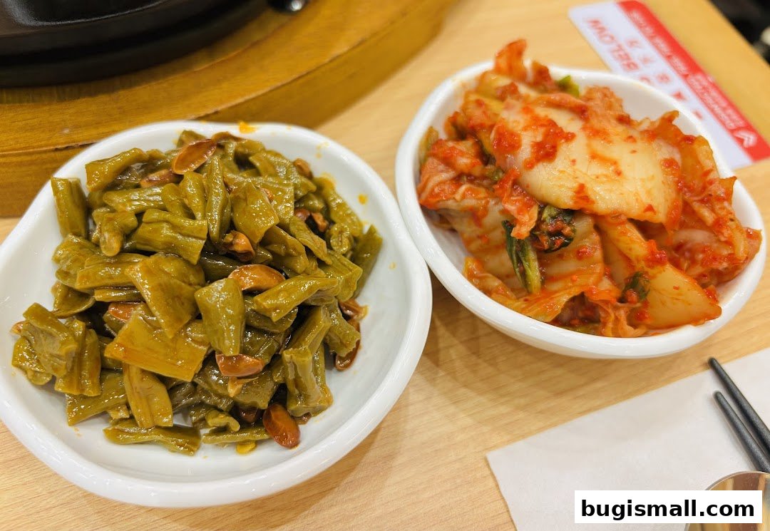 Two bowls of Korean side dishes, kimchi and stir-fried green beans, are displayed on a wooden table.