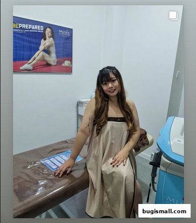 A woman sits on a treatment bed in a salon, with a promotional poster on the wall.