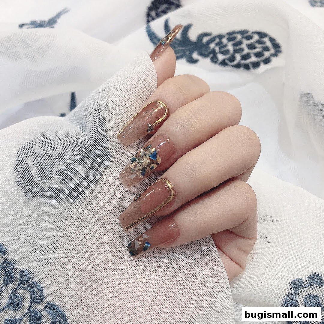A hand with long, elegant coffin-shaped nails adorned with gold accents and blue and gold embellishments.