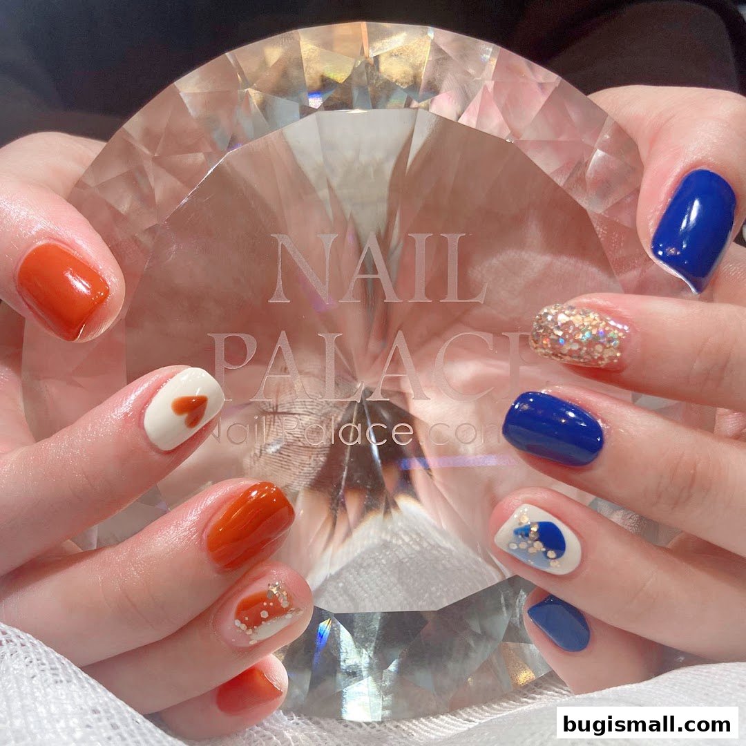 Hands showcasing beautifully designed nails with orange, white, blue, and glitter accents.