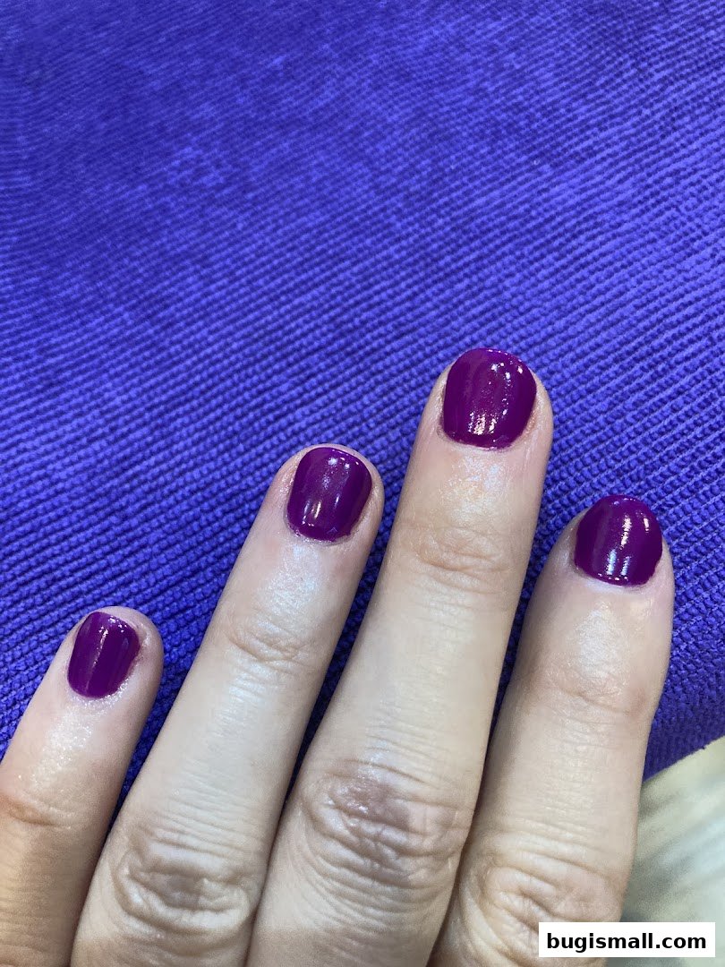Close-up of a hand with freshly painted nails in a vibrant purple shade.