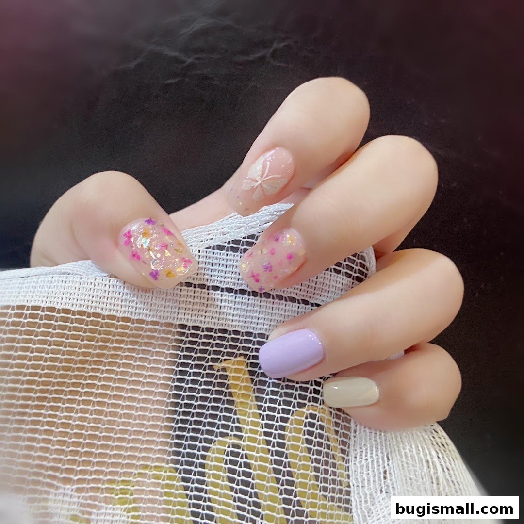 A close-up of a hand showcasing beautifully decorated nails with glitter and butterfly designs.