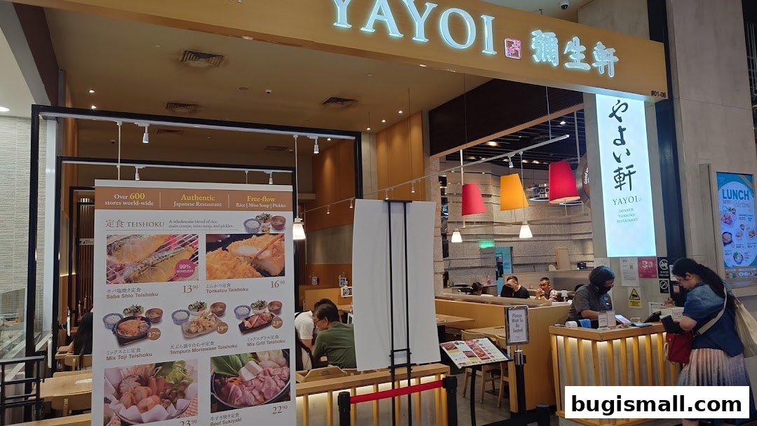 The entrance of Yayoi Japanese Teishoku Restaurant with a menu display and customers.