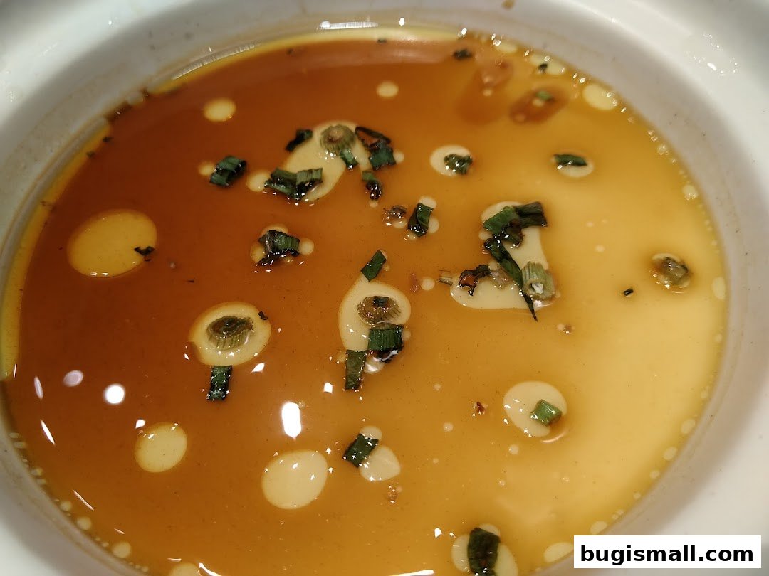 A close-up of a savory dish with broth, scallions, and oil droplets.