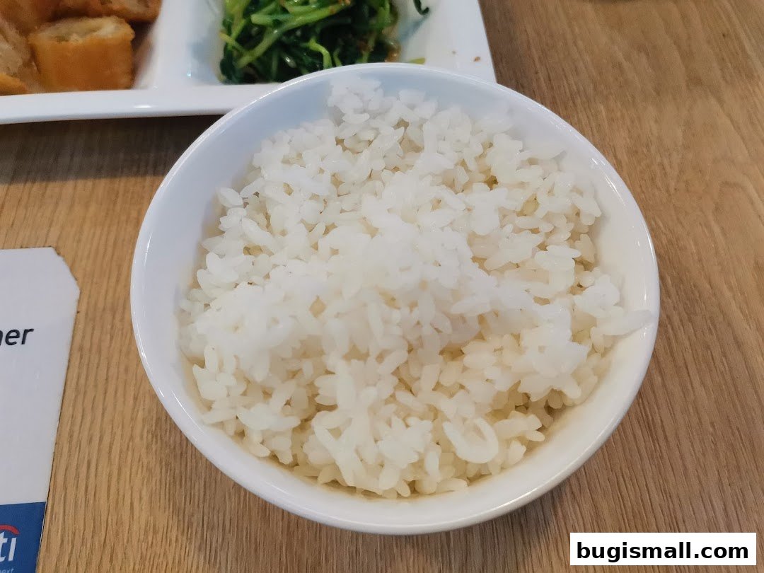 A close-up shot of a bowl of fluffy white rice, with other dishes blurred in the background.
