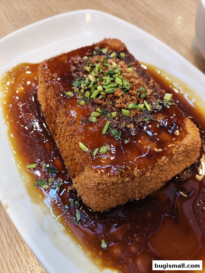 A close-up of a crispy fried tofu dish with savory sauce and green onions.