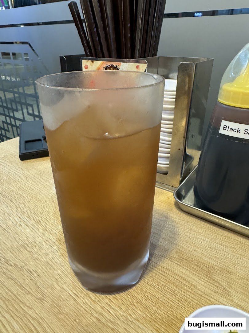 A tall glass of iced tea sits on a wooden table next to a bottle of black sauce.