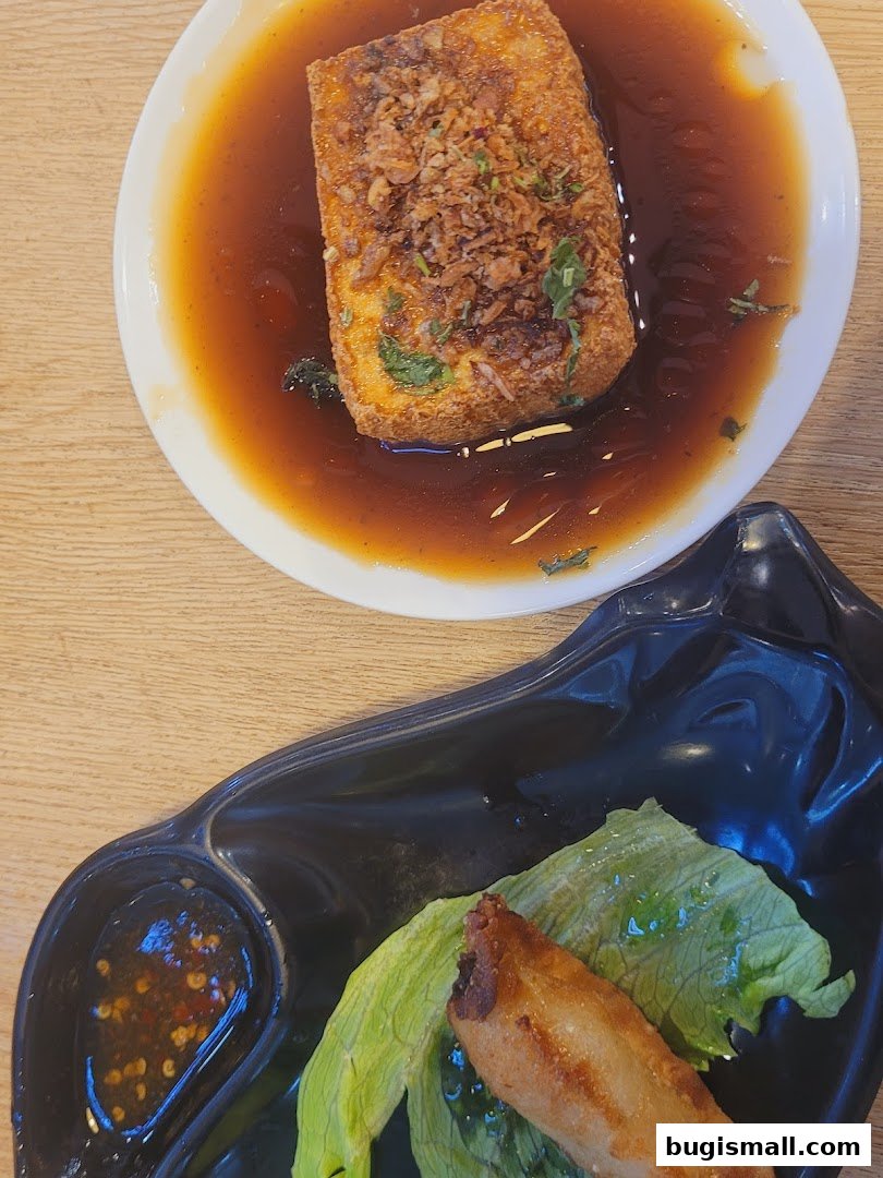 A close-up of two dishes: fried tofu in broth and a spring roll with lettuce and dipping sauce.