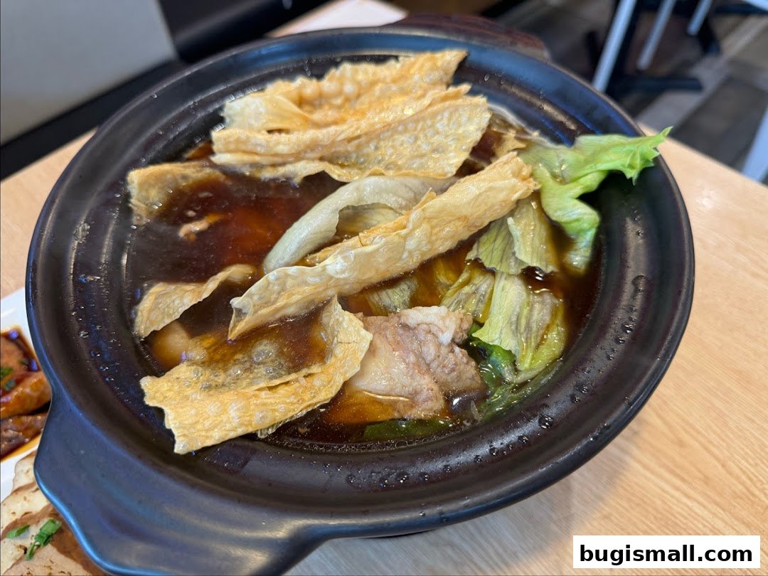 A close-up shot of a steaming bowl of Bak Kut Teh with tofu skin and vegetables.