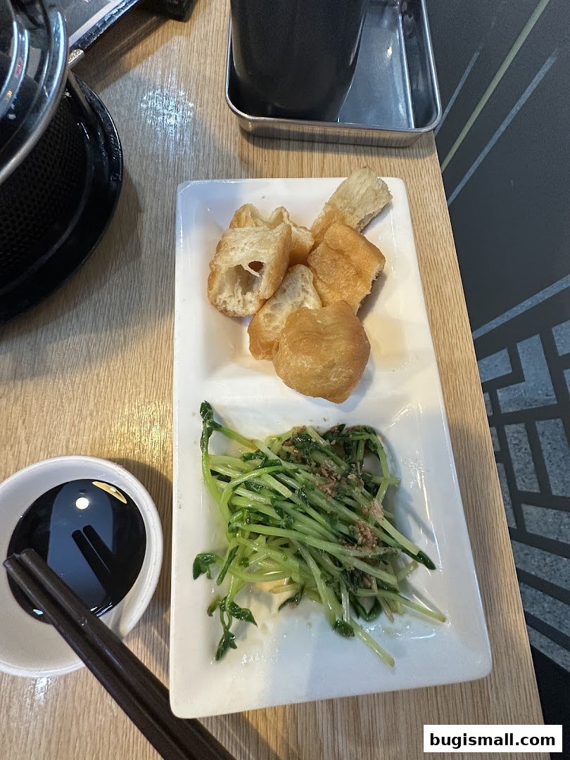 A plate of fried dough sticks and stir-fried greens with a side of dipping sauce.