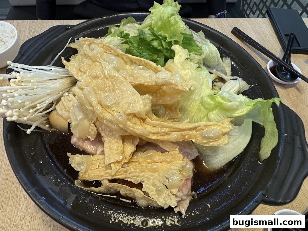 A steaming bowl of Bak Kut Teh with enoki mushrooms, tofu skin, and lettuce.