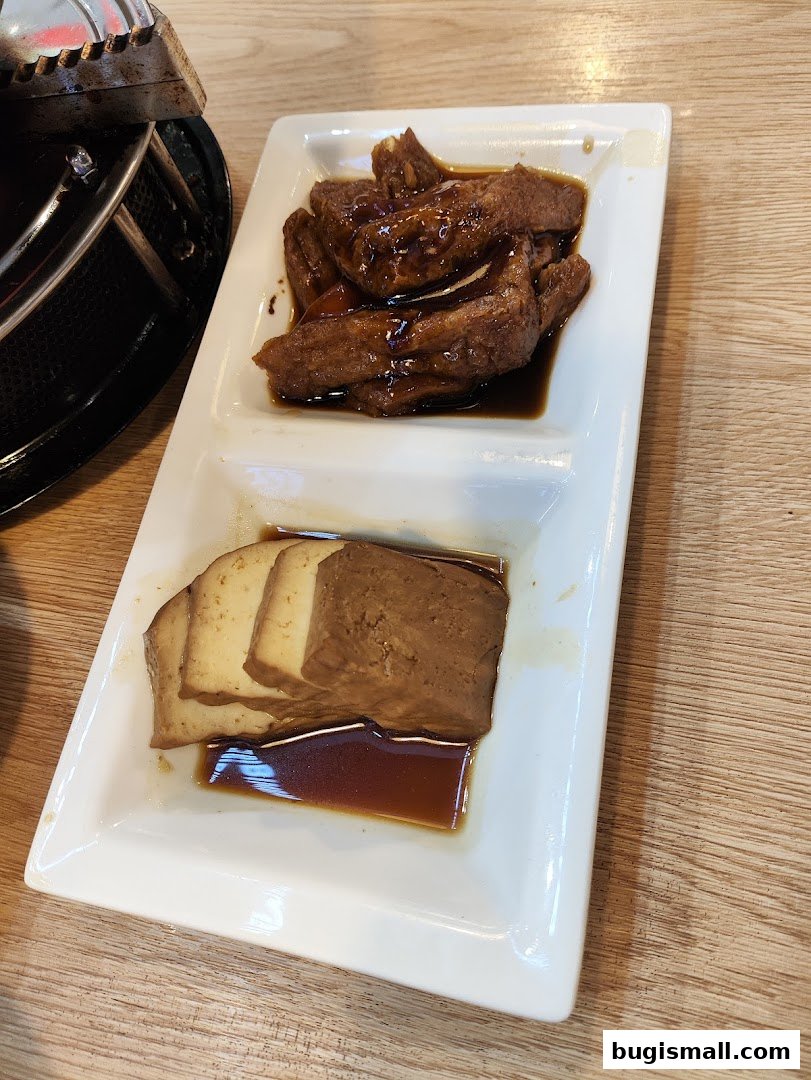 A white rectangular plate with two sections, one holding braised duck wings and the other braised tofu.