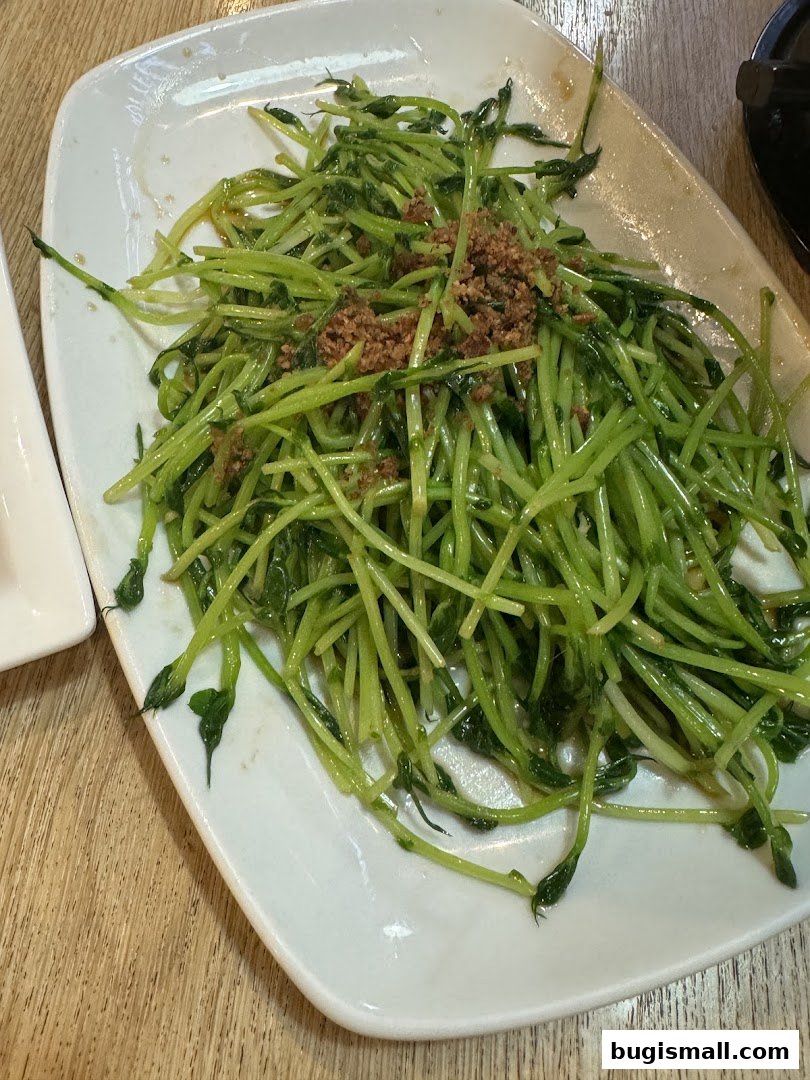 A plate of stir-fried pea shoots with garlic on a white plate.
