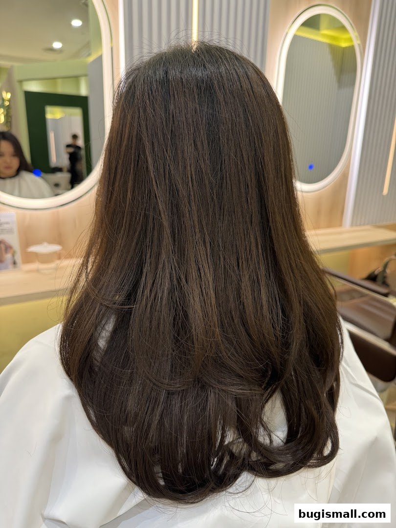 A person's back with long, dark, layered hair in a salon setting.