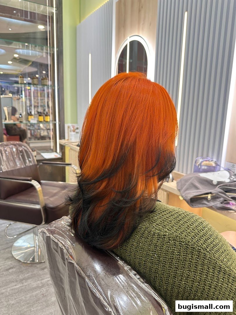 A person with vibrant orange and black ombre hair sits in a salon chair.
